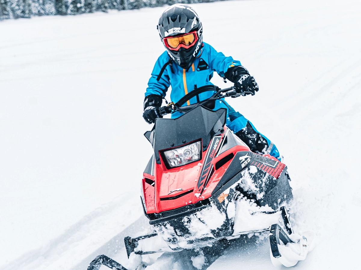 Un enfant avec casque conduit une motoneige Arctic Cat